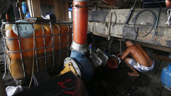 An illegal gold miner fixes a machine on a dredging barge on the Madeira river, a tributary of the Amazon river in Autazes, Amazonas state, Brazil, Thursday, Nov.25, 2021. Hundreds of mining barges have arrived during the past two weeks after rumors of gold spread, with environmentalists sounding the alarm about the unprecedented convergence of boats in the sensitive ecosystem. (AP Photo/Edmar Barros)