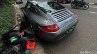 Seorang anak penjual tisu duduk di samping mobil mewah milik orang kaya Jakarta.