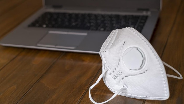 masker berkatub KN95 FPP2 Corona Virus Protection face mask on a wooden desk with a laptop computer out of focus in the background
