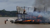 Seorang penambang ilegal menyiramkan air ke kapal untuk memadamkan api usai tongkang tersebut dibakar otoritas IBAMA di sungai Madeira, anak sungai Amazon, Brasil.