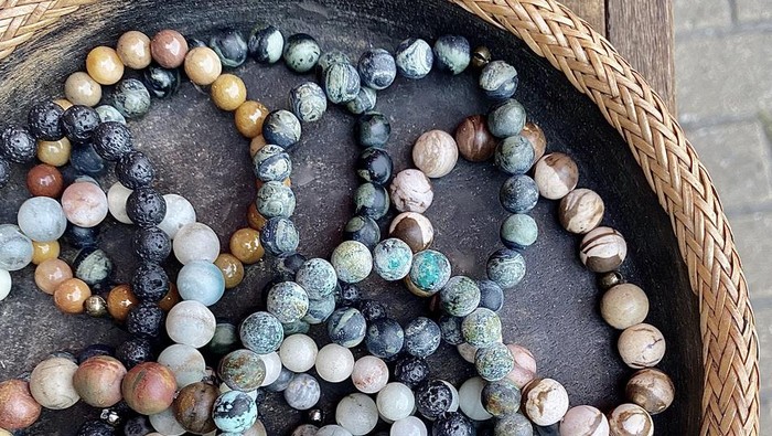 Vertical close up of art in the everyday: earth color crystal bracelets in wicker and stone basket at artisan markets Byron Bay
