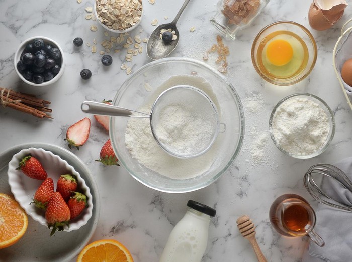 Making pancakes, cake, baking of baker hands pouring or sifting flour in bowl. Concept of Cooking ingredients and method on white marble background. Dessert recipes and homemade.