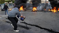 Seorang pengunjuk rasa menuangkan minyak di depan ban yang terbakar memblokir jalan raya utama yang mengarah ke bandara internasional Beirut. 