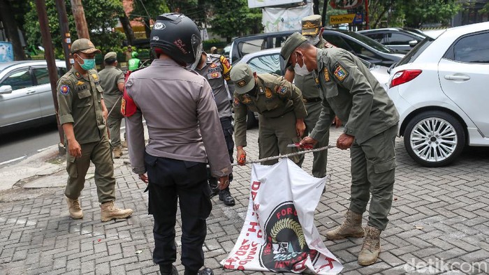 Petugas gabungan dari Satpol PP Kecamatan Cilandak, TNI dan Polisi melakukan penurunan bendera organisasi di kawasan Cilandak, Jakarta Selatan.