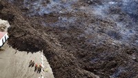 Petugas pemadam kebakaran berdiri di samping lava yang mengalir. Dalam 10 minggu sejak itu, setidaknya 11 aliran lava yang berbeda telah diidentifikasi oleh para ilmuwan, meliputi setidaknya 1.100 hektar (2.700 hektar) tanah, termasuk ribuan rumah, jalan, saluran listrik dan pipa irigasi untuk perkebunan pisang yang penting secara ekonomi di pulau itu.