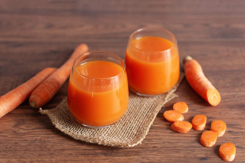 Healthy carrot juice in a glass and fresh carrots on a table. Healthy dieting drink in a glass on wooden table background.