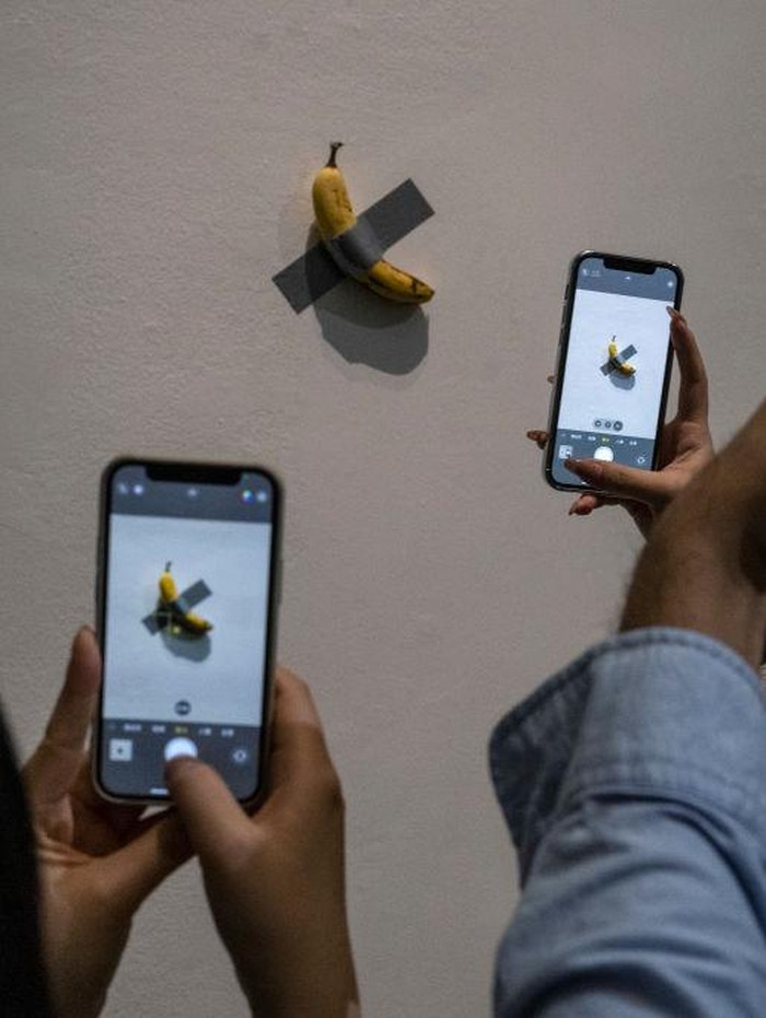 BEIJING, CHINA - NOVEMBER 28: Visitors take pictures of  the work Comedian by Italian artist Maurizio Cattelan that is part of his exhibition The Last Judgement at the UCCA Center for Contemporary Art on November 28, 2021 in Beijing, China. The show, which displays work from three decades of Cattelan artists career, is his first solo exhibition in mainland China. Widely regarded for his hyperrealist sculptures and installations, one of his most famous works is a banana duct taped to a wall known as Comedian. (Photo by Kevin Frayer/Getty Images)