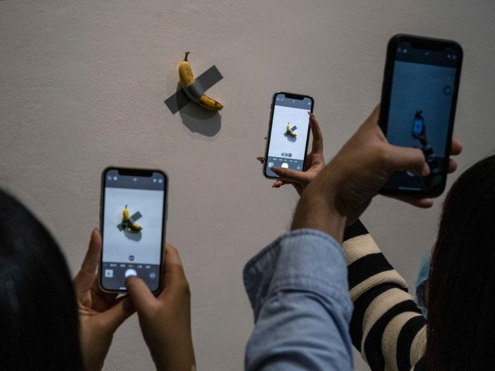 BEIJING, CHINA - NOVEMBER 28: Visitors take pictures of  the work Comedian by Italian artist Maurizio Cattelan that is part of his exhibition The Last Judgement at the UCCA Center for Contemporary Art on November 28, 2021 in Beijing, China. The show, which displays work from three decades of Cattelan artists career, is his first solo exhibition in mainland China. Widely regarded for his hyperrealist sculptures and installations, one of his most famous works is a banana duct taped to a wall known as Comedian. (Photo by Kevin Frayer/Getty Images)
