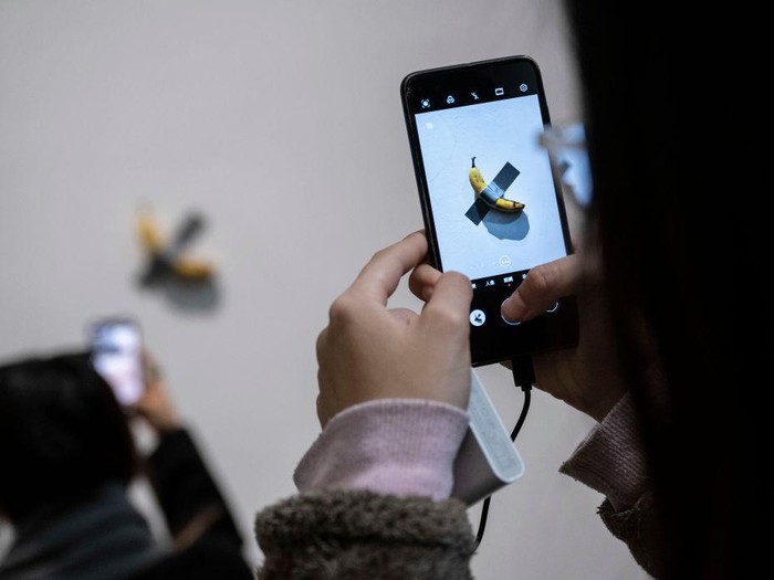 BEIJING, CHINA - NOVEMBER 28: Visitors take pictures of  the work Comedian by Italian artist Maurizio Cattelan that is part of his exhibition The Last Judgement at the UCCA Center for Contemporary Art on November 28, 2021 in Beijing, China. The show, which displays work from three decades of Cattelan artists career, is his first solo exhibition in mainland China. Widely regarded for his hyperrealist sculptures and installations, one of his most famous works is a banana duct taped to a wall known as Comedian. (Photo by Kevin Frayer/Getty Images)