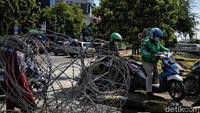 Terlihat warga mencoba memaksa melewati kawat duri melalui celah di ujung trotoar.