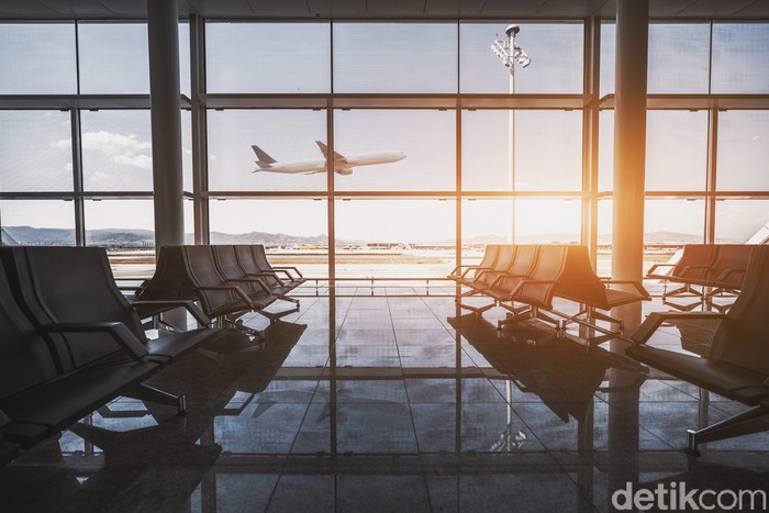 Wide-angle view of a modern aircraft gaining the altitude outside the glass window facade of a contemporary waiting hall with multiple rows of seats and reflections indoors of an airport terminal El Prat in Barcelona