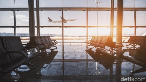 Wide-angle view of a modern aircraft gaining the altitude outside the glass window facade of a contemporary waiting hall with multiple rows of seats and reflections indoors of an airport terminal El Prat in Barcelona