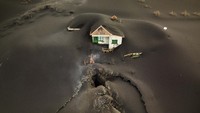 Sebuah lubang menganga di depan rumah warga yang tertutup debu. Para ahli vulkanologi menyakini celah ini sempat menyemburkan lava.