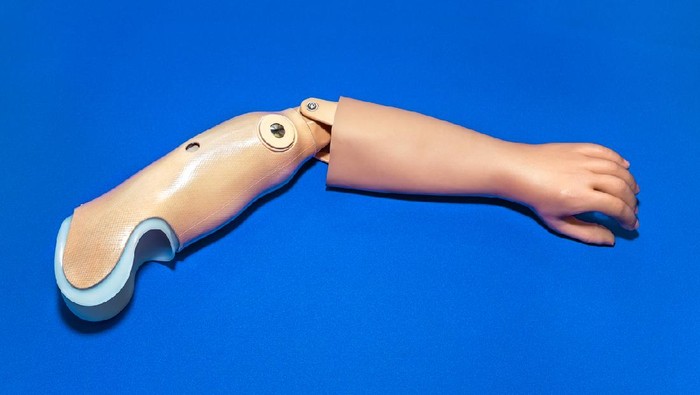 Single prosthetic arm in light skin tone color over isolated blue background.