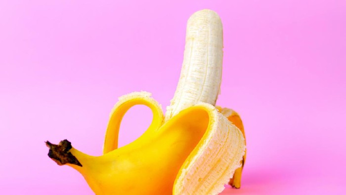 An open banana symbolizing the male sexual organ in an erect state. Pink background. Concept of potency and mens health and strength. Copy space.