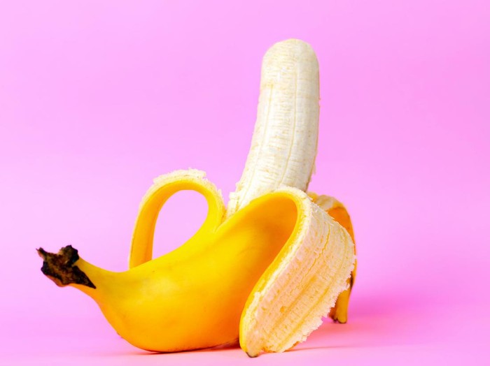 An open banana symbolizing the male sexual organ in an erect state. Pink background. Concept of potency and mens health and strength. Copy space.