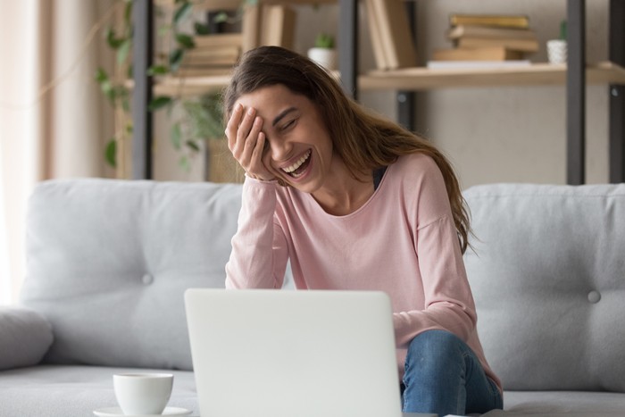 Laughing woman sitting on sofa watch comedy movie on pc enjoy funny videos stand up show online program listens comic feels overjoyed, weekend activities at home, wireless tech internet usage concept