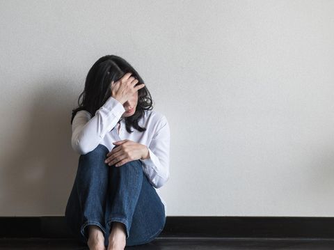 Anxiety disorder menopause woman, stressful depressed, panic attack person with mental health illness, headache and migraine sitting with back against wall on the floor in domestic home