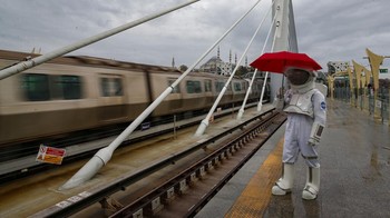 Pakai payung, seorang pria berpakaian astronaut menunggu kereta di stasiun MRT Halic. Acara ini juga akan menunjukkan bagaimana penelitan ruang angkasa telah berkembang secara historis baik di Turki maupun di seluruh dunia.
