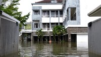 Warga berjalan menerobos banjir yang menggenangi apartemen di kawasan Legian.