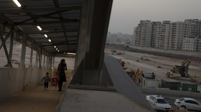 FILE - A woman and her child walk on a pedestrian ramp to the Qalandia checkpoint to the West Bank from Jerusalem, next to the site where Israel planned to build a massive Jewish settlement on the site of a long-abandoned airport, Nov. 24, 2021. An Israeli monitoring group said Monday, Dec. 6, 2021, that Jerusalem municipal officials have frozen plans to build a large Jewish settlement at the abandoned airport in east Jerusalem in the wake of heavy U.S. opposition to the project. (AP Photo/Maya Alleruzzo, File)