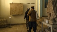 Pengunjung berjalan di depan batu kapur AC abad kedua dalam Bahasa Baktria dengan tulisan Yunani di Museum Nasional Afghanistan, di Kabul.