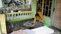 Dengan menggunakan sapu lidi dan air, keduanya telaten membersihkan abu vulkanik yang memenuhi lantai rumah.
