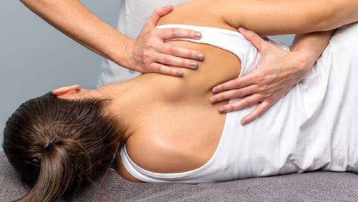 1252775797 A physical therapist stretches a female patients leg or hip as she lies on a treatment table in a clinical setting. Both the therapist and the patient are wearing protective masks to prevent the spread of infectious diseases.