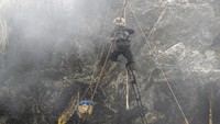 Pemburu madu memberi isyarat kepada rekan setimnya untuk menggunakan tali yang diikat ke keranjang, penuh dengan sarang yang menetes, untuk menurunkannya ke tanah.