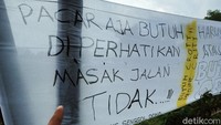 Pada spanduk kain putih itu terdapat kalimat yang dituliskan dengan spidol hitam. Di antaranya Pacar saja butuh diperhatikan masak jalan tidak, Haruskah tahun depan janji baru akan datang, dan Butuh 6 km bukan 1,5 km,.