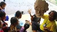 Anak-anak mendengarkan cerita boneka kardus oleh pegiat literasi Bahana Patria Gupta di depan pengungsian bencana letusan Gunung Semeru, SDN Supiturang 4, Pronojiwo, Lumajang, Jawa Timur, Kamis (9/12/2021).