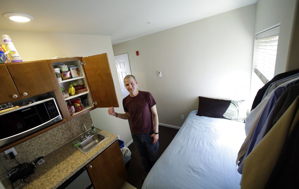 In this photo taken Wednesday, April 24, 2013, Kris King spreads stands in the kitchen, which is adjacent to the bed which is next to an open closet, in his tiny apartment in Seattle. Even King was initially shocked by the size of the apartment he rented near downtown, roughly the size of large parking spot. Cities such as San Francisco, New York and Boston have been encouraging tiny apartments to cater to young workers, retirees others who prefer city dwelling, singles or students. San Francisco last fall approved construction of apartments as small as 220 square feet, while Boston has approved 300 new units as small as 375 sq. feet. But in Seattle, where city codes have allowed for even smaller micro-apartments and dozens have been built in the last five years, the trend is facing a backlash from some neighbors who are pushing for a building moratorium or for them to be more adequately regulated. (AP Photo/Elaine Thompson)