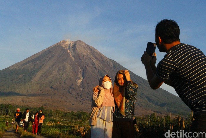STATUS GUNUNG SEMERU MASIH WASPADA Warga berfoto dengan latar belakang gunung Semeru terlihat di desa Supiturang, Pronojiwo, Lumajang, Jawa Timur, Jumat (10/12/2021). Pusat Vulkanologi Mitigasi Bencana Geologi (PVMBG) mencatat dalam laporan per enam jam, gunung Semeru masih berada di status Waspada (level 2) dengan aktivitas awan panas serta kegempaan sebanyak tiga kali dengan amplitudo 2-6 mm dan satu kali gempa vulkanik dalam. ANTARA FOTO/Ari Bowo Sucipto/aww.