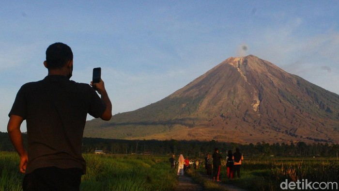 Warga berfoto dengan latar belakang gunung Semeru terlihat di desa Supiturang, Pronojiwo, Lumajang, Jawa Timur, Jumat (10/12/2021). Pusat Vulkanologi Mitigasi Bencana Geologi (PVMBG) mencatat dalam laporan per enam jam, gunung Semeru masih berada di status Waspada (level 2) dengan aktivitas awan panas serta kegempaan sebanyak tiga kali dengan amplitudo 2-6 mm dan satu kali gempa vulkanik dalam.   ANTARA FOTO/Ari Bowo Sucipto/aww.