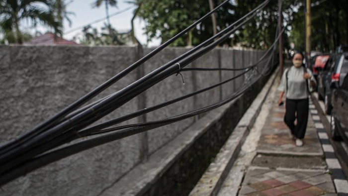 Seorang pejalan kaki melintas di trotoar yang terdapat kabel menjuntai di Jalan TMP Taruna, Kota Tangerang, Banten, Senin (13/12/2021). Selain dapat mengganggu fungsi trotoar, kabel yang terjuntai tersebut juga dapat membahayakan para pejalan kaki yang melintas. ANTARA FOTO/Fauzan/wsj.