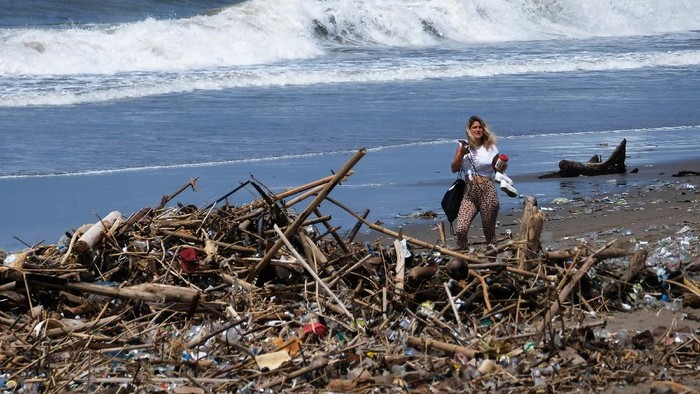 SAMPAH DI KAWASAN PARIWISATA BALI Pekerja mempersiapkan payung untuk tempat bersantai bagi wisatawan di dekat tumpukan sampah yang berserakan di sepanjang Pantai Berawa, Kuta Utara, Badung, Bali, Minggu (12/12/2021). Sampah tersebut terbawa arus laut yang kemudian terdampar sehingga mencemari kawasan pariwisata. ANTARA FOTO/Nyoman Hendra Wibowo/tom.