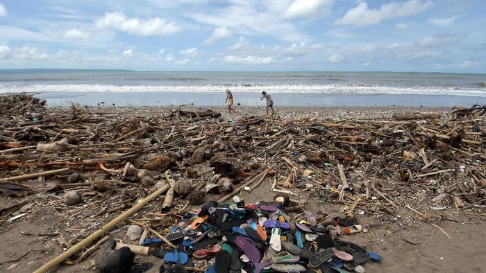 Pekerja mempersiapkan payung untuk tempat bersantai bagi wisatawan di dekat tumpukan sampah yang berserakan di sepanjang Pantai Berawa, Kuta Utara, Badung, Bali, Minggu (12/12/2021). Sampah tersebut terbawa arus laut yang kemudian terdampar sehingga mencemari kawasan pariwisata. ANTARA FOTO/Nyoman Hendra Wibowo/tom.