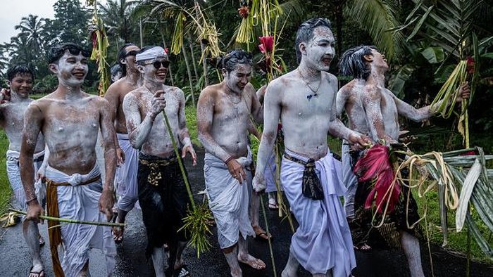 Tradisi Mewarnai Diri Untuk Mengusir Roh Jahat di Bali GIANYAR, BALI, INDONESIA - DECEMBER 15: Balinese boys with apply white body paint walk under the rain during the sacred Ngerebeg Ritual on December 15, 2021 in Tegalalang Village Gianyar, Bali, Indonesia. In a tradition that bears similarity to Halloween, boys paint their bodies and faces in menacing patterns to partake in Ngerebeg, a ritual held every six months to pacify local spirits. The ritual features a raucous street parade of the painted youths, who are supposed to resemble the supernatural beings and demons of Balinese beliefs. (Photo by Agung Parameswara/Getty Images)