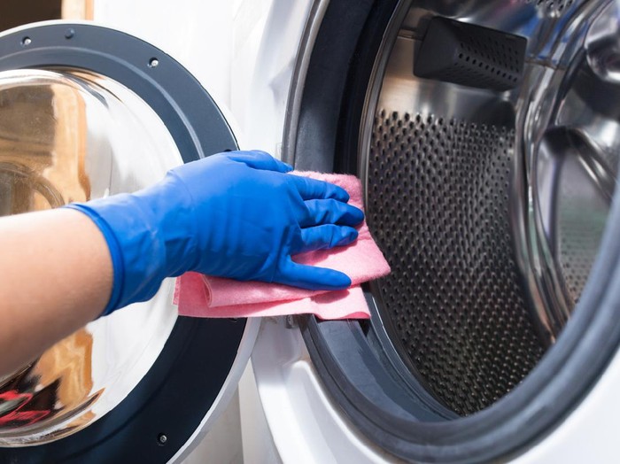 Hand in blue glovesw cleaning washing mashine with piece of cloth