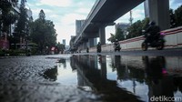 Saat hujan, air menggenang di jalan yang rusak.