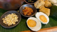 Rawonnya ditempatkan di kendi tanah liat, kemudian dikelilingi pelengkap seperti kecambah, sambal merah, telur asin, dan kerupuk. Lalu ada juga menu pendamping, tahu crispy plus cocolan saus kecap cabe rawit.