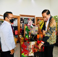 Jokowi yang didampingi Menteri Sekretaris Negara Pratikno lantas mencoba jaket tersebut. Jaket itu berwarna hitam dengan lukisan bergambar Garuda Pancasila, penari tayub khas Blora, berikut motif bercorak daun jati. Peletakan lukisan yang secara asimetris menciptakan kesan modern. (Foto: Dok. BPMI Sekretariat Presiden)