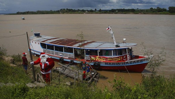 Kostum merah-putihnya sangat kontras dengan warna hijau zamrud dari hutan tropis terbesar di dunia dan perairan coklat berlumpur dari Sungai Solimoes, yang mengalir ke Amazon. AP Photo/Edmar Barros.