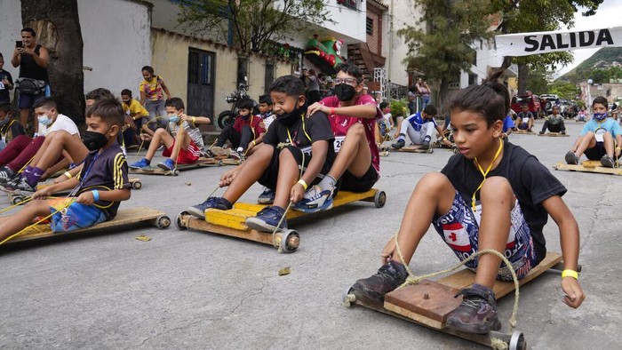 Sejumlah anak ikut serta dalam balapan di Caracas, Venezuela. Bukan naik mobil balap, mereka justru balapan dengan menaiki papan kayu beroda. Penasaran?