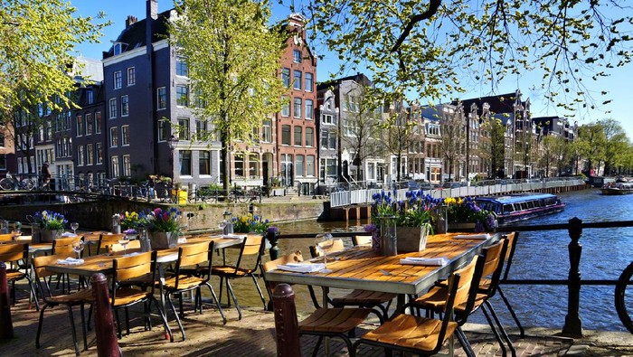 Restaurant tables lining the beautiful canals of Amsterdam under blue skies during springtime, Netherlands