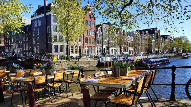 Restaurant tables lining the beautiful canals of Amsterdam under blue skies during springtime, Netherlands