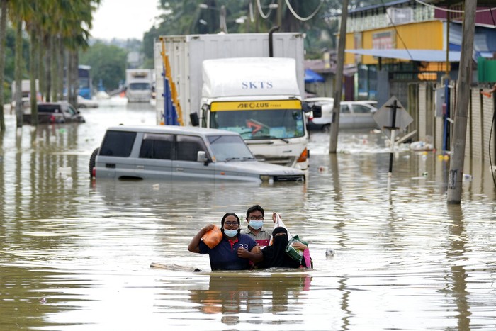Warga mengarungi jalan yang banjir di Shah Alam, di pinggiran Kuala Lumpur, Malaysia, Senin, 20 Desember 2021. Layanan penyelamatan pada Senin bekerja untuk membebaskan ribuan orang yang terjebak banjir terparah Malaysia dalam beberapa tahun setelah hujan lebat berhenti menyusul lebih banyak lagi. dari tiga hari hujan deras di ibu kota dan di seluruh negeri. (Foto AP/Vincent Thian)