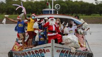 Santa Klaus itu melambaikan tangan dengan riang kepada anak-anak yang menunggunya di tepi sungai. AFP/MICHAEL DANTAS.