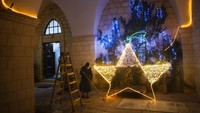 Seorang biarawati membersihkan lantai setelah mendekorasi pintu masuk gereja dengan lampu Natal, di Kota Tua Yerusalem, Minggu, (12/12/2021). (AP Photo/Oded Balilty)