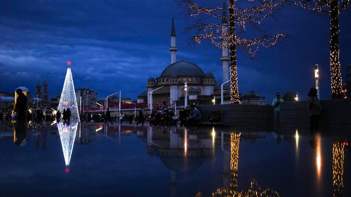 Gemerlap Sambut Natal Dunia Pejalan kaki berjalan melewati pohon Natal di samping masjid Taksim di Taksim square di Istanbul, Turki, Jumat, 10 Desember 2021. (AP Photo/Francisco Seco)